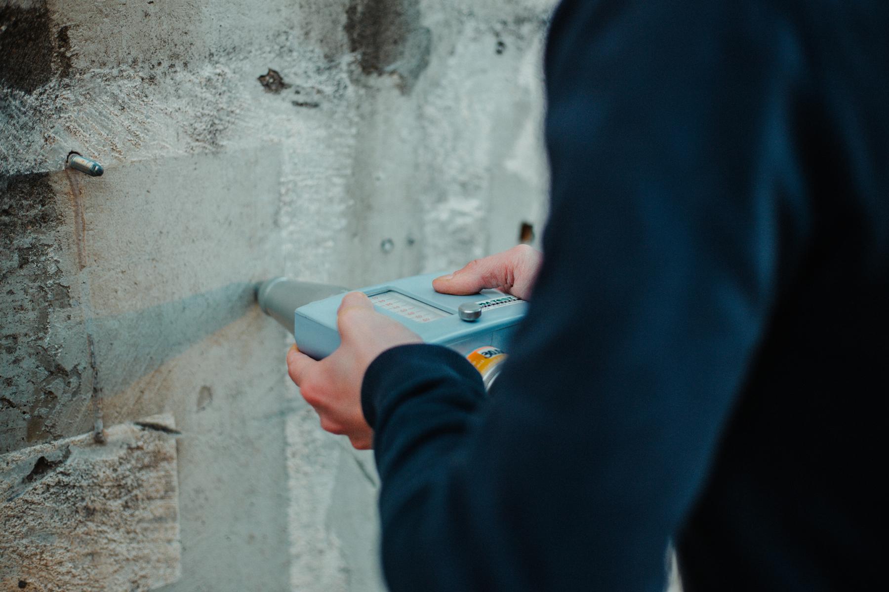 Die Aufnahme zeigt die zerstörungsfreie Bestimmung der Rückprallzahl mithilfe eines Schmidt-Hammers an einer Betonwand. Anhand der ermittelten Rückprallzahlen können Rückschlüsse auf die Betongüte bzw. die Druckfestigkeit gezogen werden.