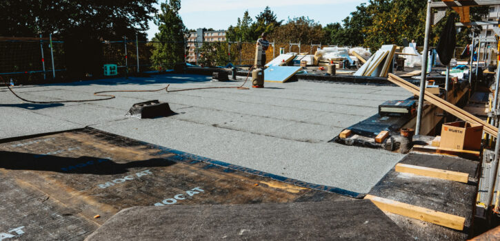 Das Bild zeigt im Rahmen der Bauleitung die Sanierung eines Flachdachs, wo gegenwärtig der Einbau von Dämmstoffeinlagen und die Applikation von Bitumenbahnen zu beobachten ist.
