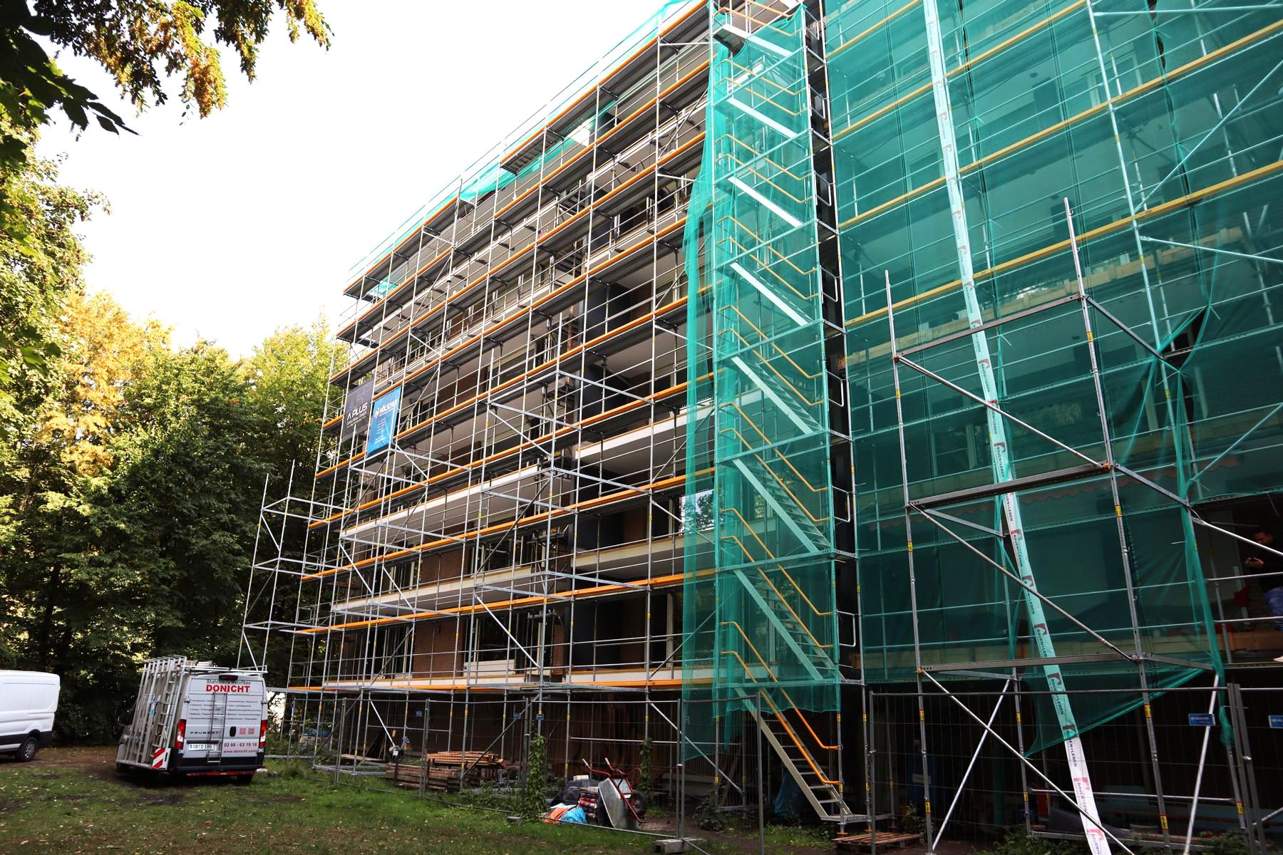 Das Bild zeigt die Rückseite eines Mehrfamilienhauses, an der im Zuge einer Balkonsanierung (Bausanierung) eine Gerüststellung erfolgte. Die Balkonsanierung umfasst die nachträgliche Abdichtung der Balkontragplatten sowie intensive Betonsanierungsarbeiten.