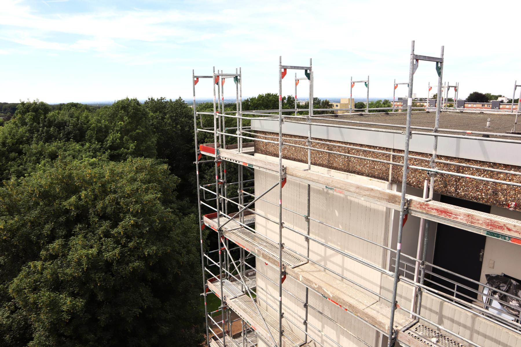 Fassadensanierung eines Hochhauses in Hilden Das Bild zeigt den Dachbereichs eines Hochhauses, dessen Fassade (aufgrund diverser Undichtigkeiten) saniert wird. Die Gerüststellung an der Fassade reicht bis über die Attika des Gebäudes hinaus. Die KKOe Beratende Ingenieure bzw. deren Bauleiter überwachten die handwerklichen und bautechnischen Arbeiten an der Fassade.