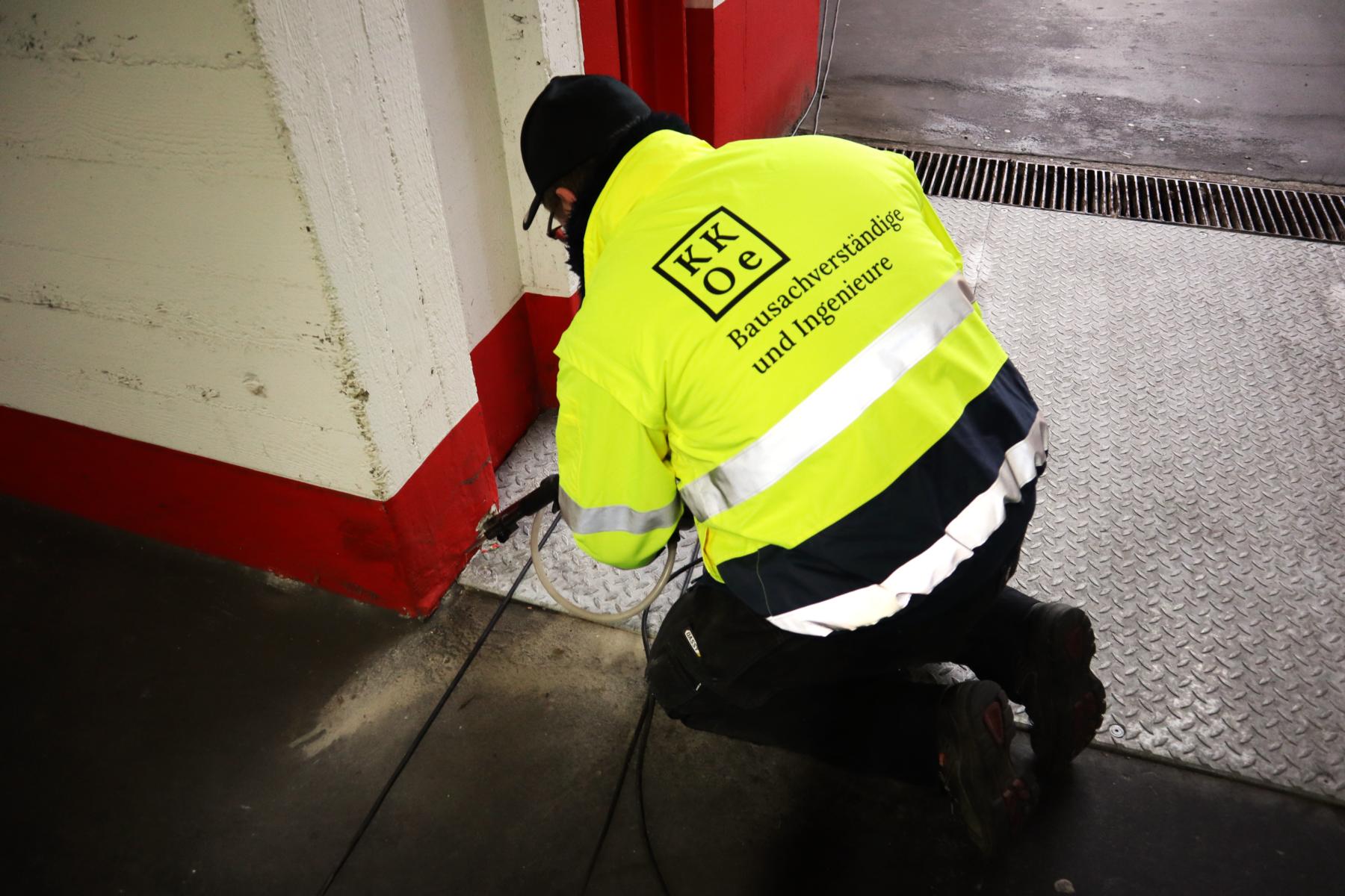Bohrmehlprobenentnahme aus einem Stahlbetonbauteil zwecks Feststellung, ob eine chloridinduzierte Bewehrungskorrosion eingesetzt hat Das Bild zeigt einen Mitarbeiter der KKOe Beratende Ingenieure PartG mbB, der im Rahmen einer Bauwerksdiagnostik (auch: Bauwerksuntersuchung oder in diesem Fall eine Tiefgaragenuntersuchung) mittels eines Spezialbohrgeräts sogenannte Bohrmehlproben aus einem Stahlbetonbauteil entnimmt. Die entnommenen Bohrmehlproben werden anschließend von einem Labor auf ihren Gesamtchloridgehalt geprüft. Dieser wiederum wird (zusammen mit anderen Untersuchungsergebnissen) von Ingenieuren der KKOe in Gutachten verarbeitet, sodass der Auftraggeber Auskunft über den technischen IST-Zustand seiner Konstruktion erhält. Das wiederum hilft bei der Planung einer Tiefgaragensanierung.