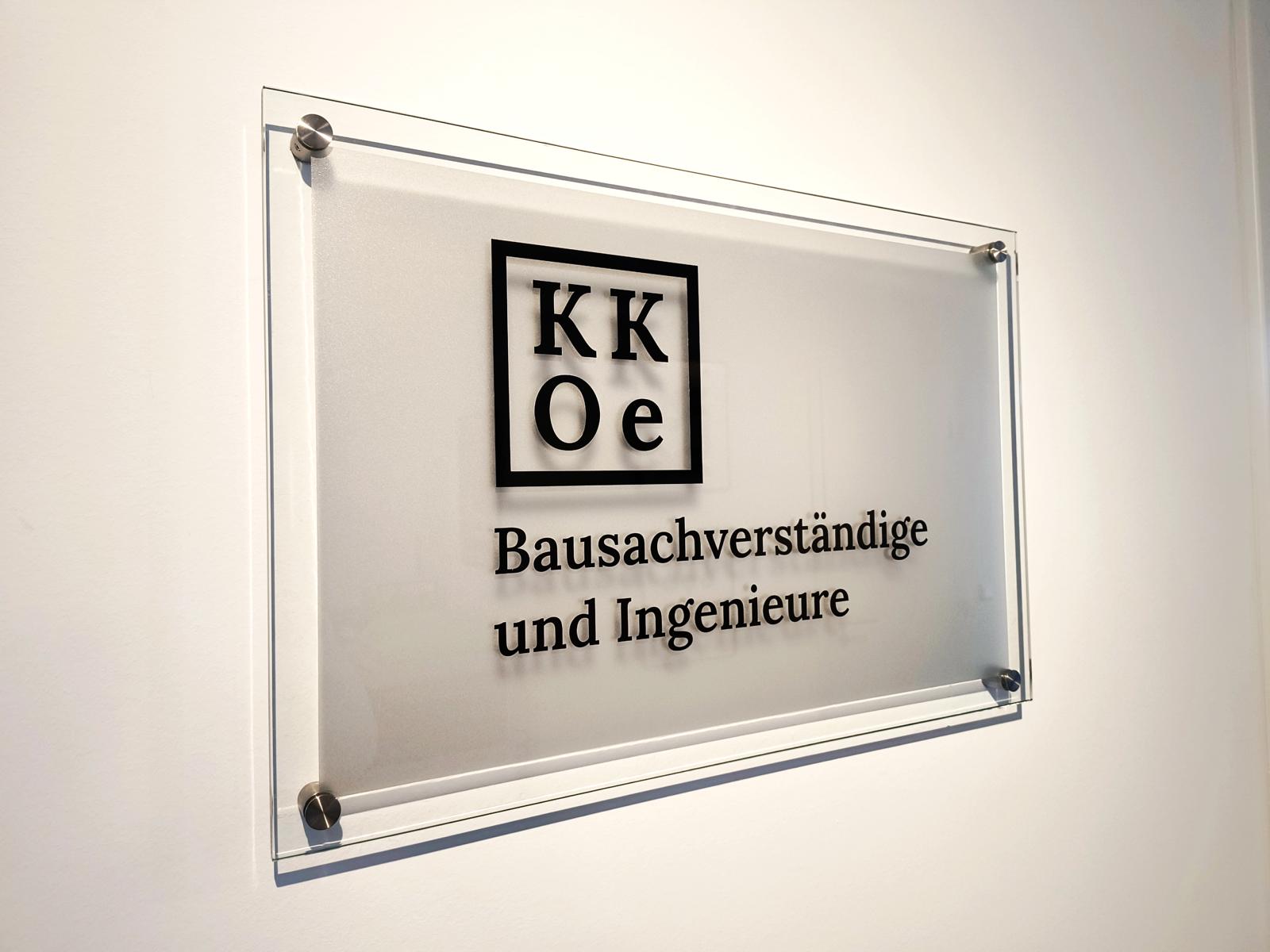Das Bild zeigt das Firmenlogo des Ingenieurbüros (Düsseldorf) der KKOe Beratende Ingenieure Kempis Kleisa PartG mbB. Dieses hängt (in Form eines Glasschildes) an der Wand im Eingangsbereich des Unternehmens.