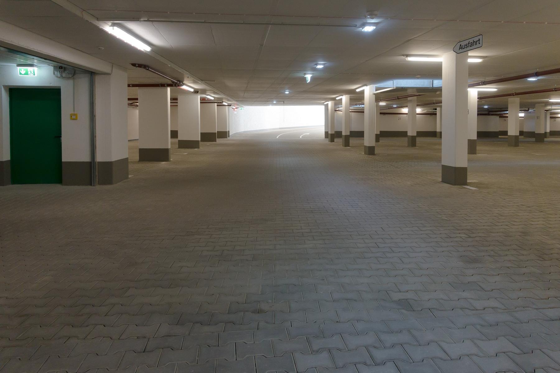 Das Bild zeit eine Tiefgarage, deren Bodenbelag aus Betonverbundsteinen ("Knochensteine") besteht. Es sin derzeit keine Autos in der Tiefgarage geparkt. Die Stahlbetonstützen des Bauwerks wurden mittels eines Oberflächenschutzsystems (d. h. einer Abdichtung) vor dem Einfluss von Tausalzen (welche durch die verkehrenden Fahrzeuge im Winter eingeschleppt werden) geschützt. Das Bild steht symbolisch für eine erfolgreiche Tiefgaragensanierung.