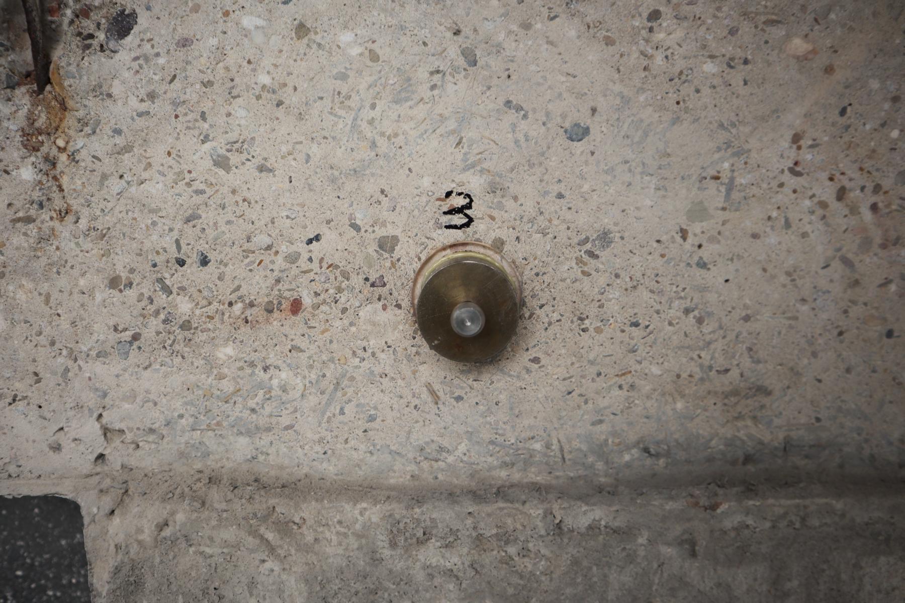 Prüfstelle vor Ermittlung der Oberflächenzugfestigkeit: auf dem Beton aufgeklebter Prüfstempel Das Bild zeigt eine vorbereitete Prüfstelle eines oberflächennahen Betons, dessen Oberflächenzugfestigkeit im Rahmen einer Bauwerksuntersuchung ermittelt werden soll. Zu erkennen ist der auf dem Beton aufgeklebte Prüfstempel einschließlich einer gebohrten Ringnut (die den Stempel wie eine Art Burggraben umgibt).