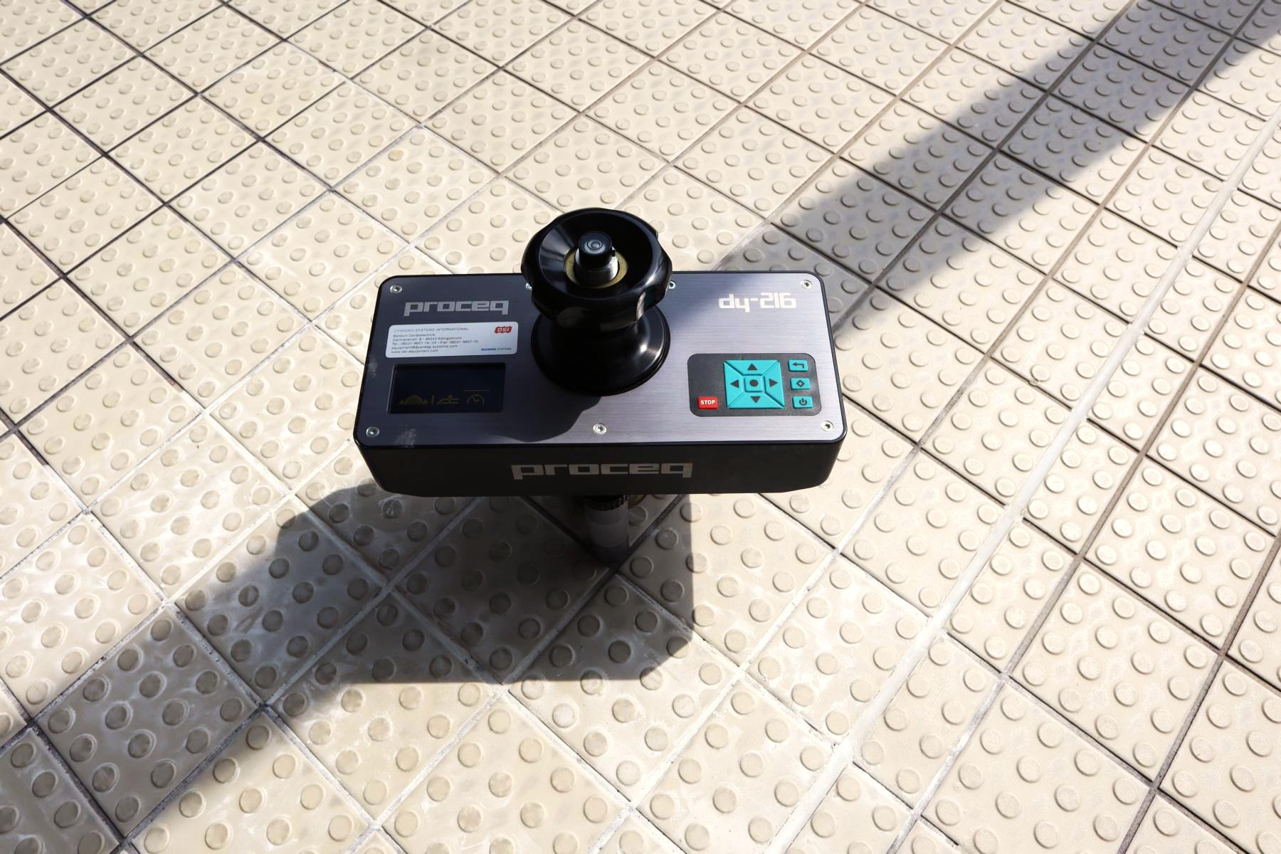 Ausgerichtetes Prüfgerät zur Feststellung der Haftzugfestigkeit eines Fliesenbelags Das Bild zeigt ein fachgerecht ausgerichtetes Prüfgerät zur Feststellung der Haftzugfestigkeit eines Fliesenbelags im Saunabereich eines Wellnessbads. Im nächsten Schritt wird die Last mittels des Prüfgeräts eingeleitet, die zum Bruch in der Fliese selbst oder aber zwischen Fliese und darunterliegendem Estrich führt.