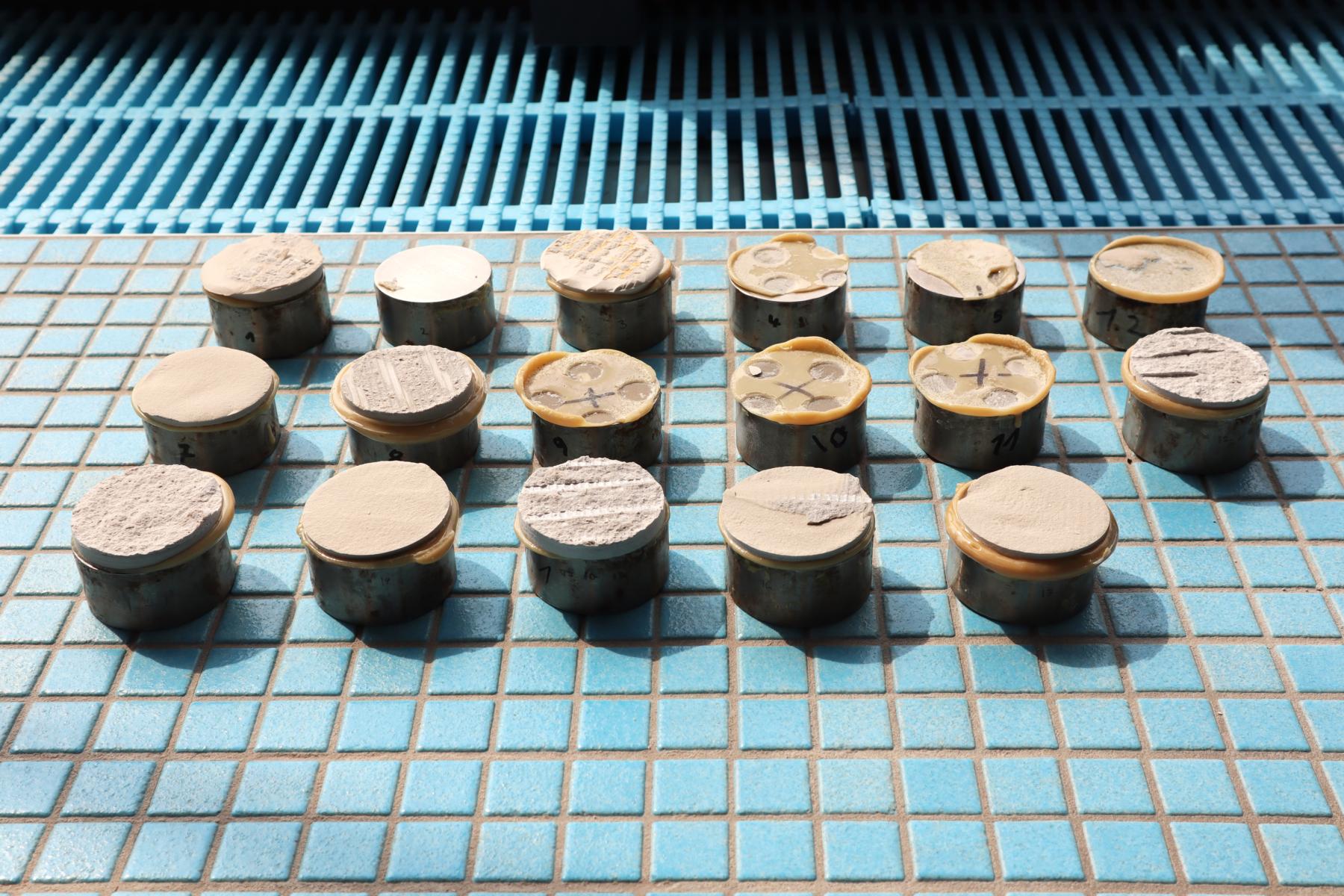 Verschiedene Bruchbilder (Kohäsions- und Adhäsionsbrüche) im Rahmen des Abreißversuchs Das Bild zeigt unterschiedliche Bruchbilder im Rahmen der Feststellung der Oberflächenzugfestigkeit und der Haftzugfestigkeit verschiedener Bauteile in einem öffentlichen Schwimmbad. Die Prüfstempel wurden von Mitarbeitern des Ingenieurbüro KKOe Kempis Kleisa PartG mbB (aus Düsseldorf, NRW) methodisch auf eine Fliesenbank gelegt, um die nach der Abreißprüfung entstandenen Bruchbilder (Kohäsions- und Adhäsionsbrüche) für ein Gutachten zu dokumentieren.