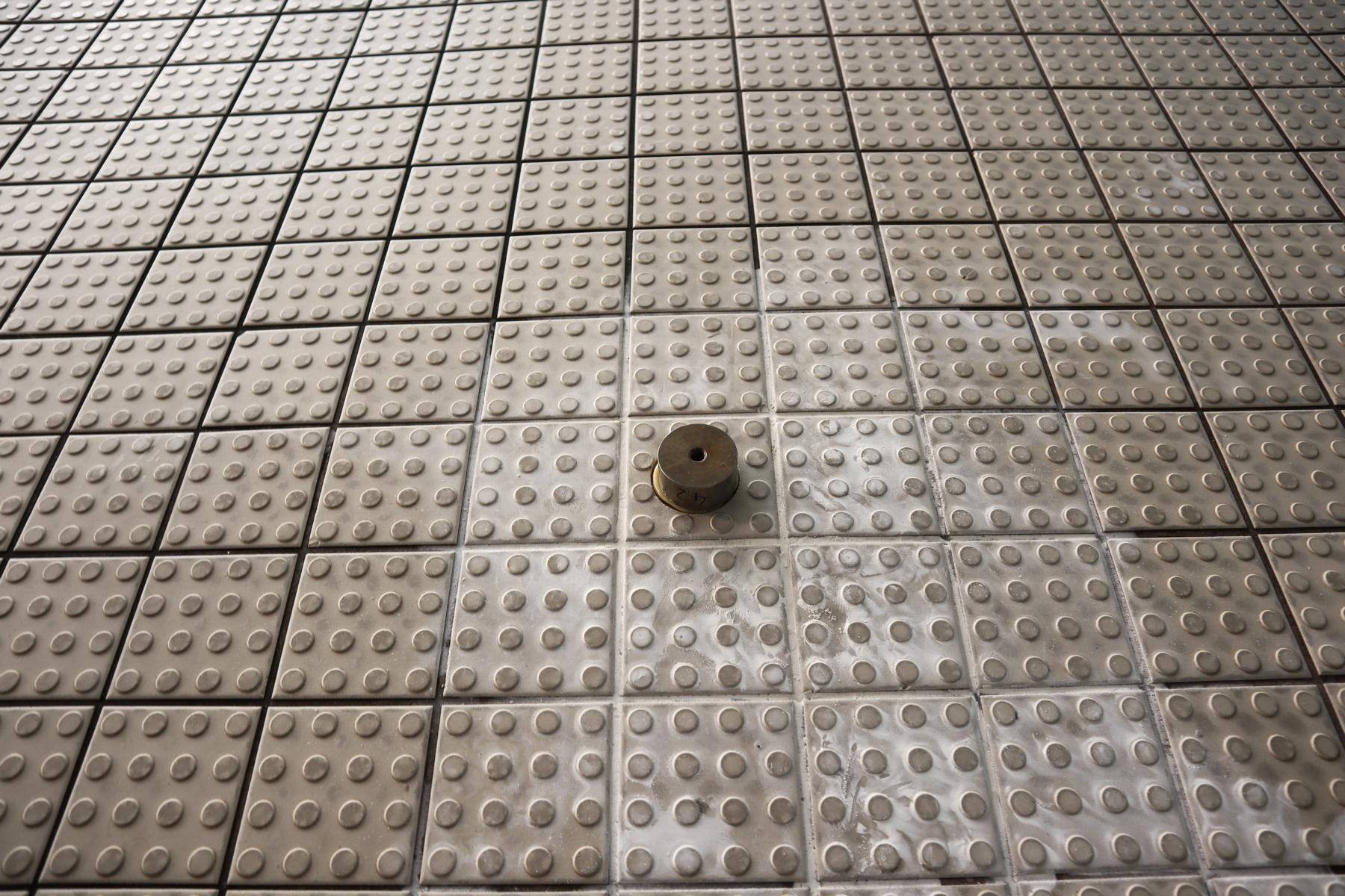 Prüfstelle vor Ermittlung der Haftzugzugfestigkeit: auf einem Fliesenbelag aufgeklebter Prüfstempel, der ein Schwimmbad umgibt Das Bild zeigt eine vorbereitete Prüfstelle eines Fliesenbelags um ein Schwimmbadbecken herum, dessen Haftzugfestigkeit im Rahmen einer Bauwerksuntersuchung ermittelt werden soll. Zu erkennen ist der auf dem Fliesenbelag aufgeklebte Prüfstempel einschließlich einer gebohrten Ringnut (die den Stempel wie eine Art Burggraben umgibt).