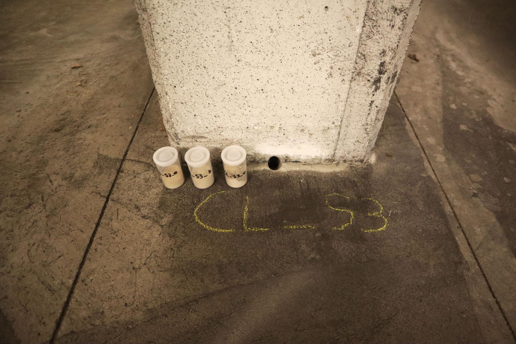 Bohrmehlentnahme aus einer Stahlbetonstütze in einem Parkhaus Das Bild zeigt eine Stahlbetonstütze in einem Parkhaus, aus der Bohrmehlproben zur Bestimmung bauschädlicher Salze entnommen wurden. Die Probendöschen im Rahmen der durchgeführten Bohrmehlentnahme stehen im Bereich des Stützenfußes.