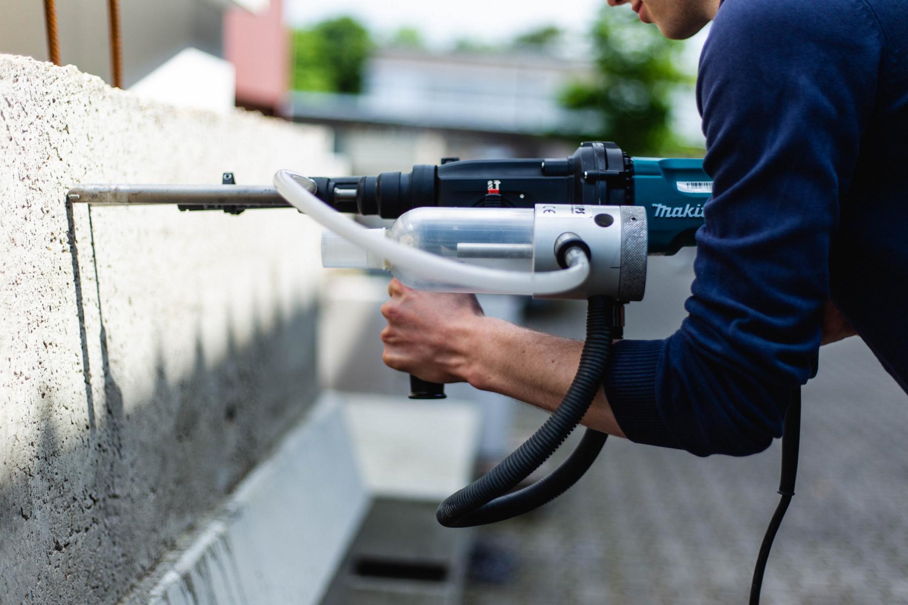Bohrmehlprobenentnahme mittels Spezialbohrgerät Das Bild zeigt eine Mitarbeiter der KKOe Beratende Ingenieure Kempis Kleisa PartG mbB, der mithilfe eines Spezialbohrgeräts Proben aus Beton entnimmt.