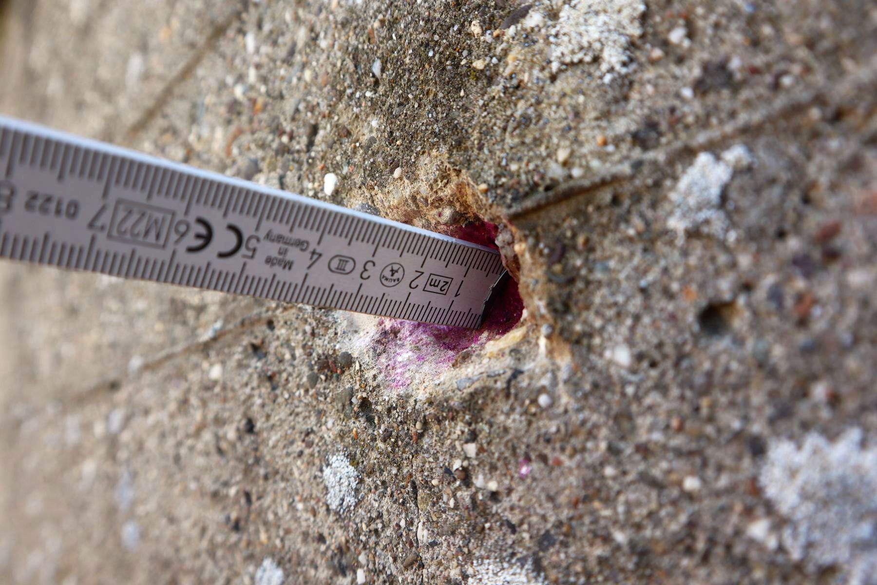 Messung des Karbonatisierungsfortschritts mit einem Zollstock und Phenolphthalein Das Bild zeigt die Prüfung und Messung der Karbonatisierung eines freibewitterten Betons mit einem Zollstock und einer Phenolphthalein-Lösung.