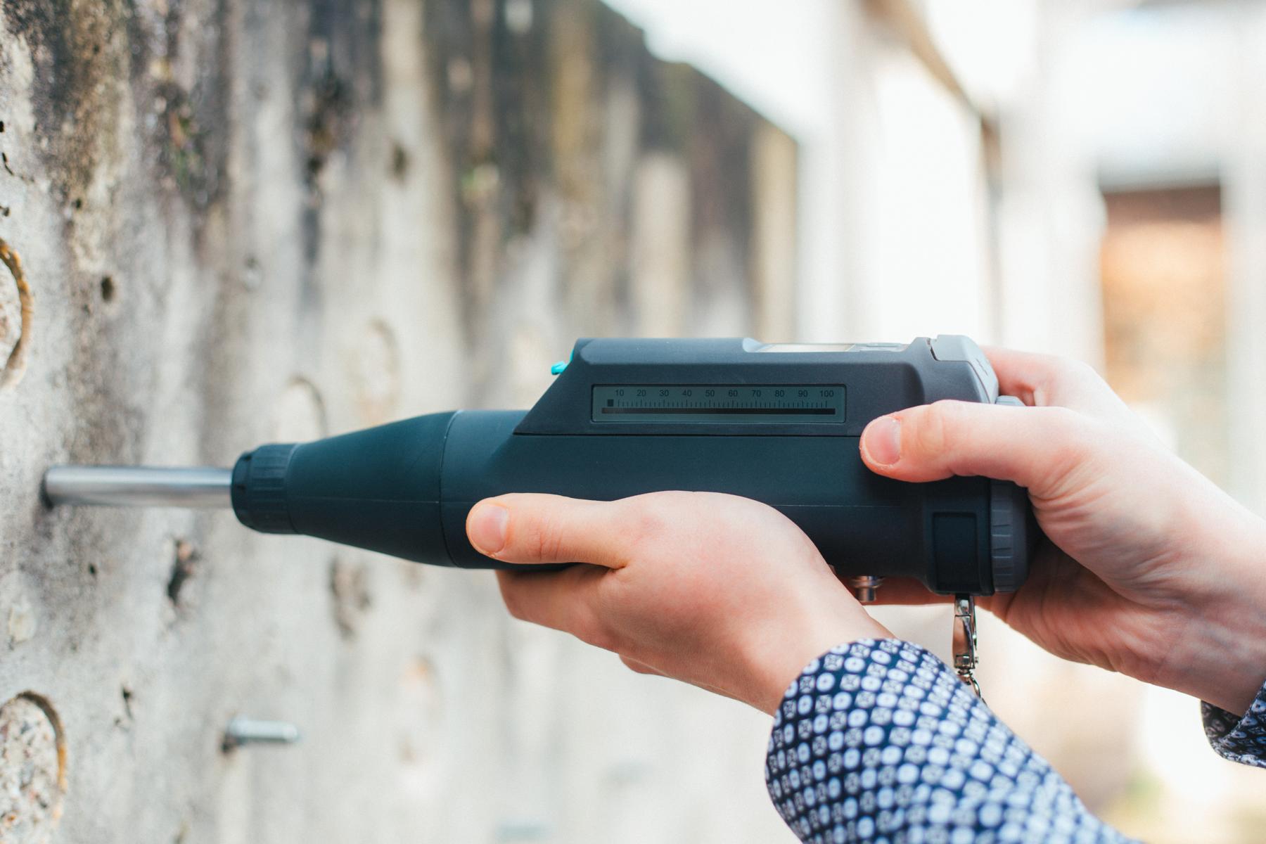 Rückprallversuch mittels eines Schmidhammers zwecks Feststellung der Druckfestigkeit eines Betons vor Ort Das Bild zeigt eine Mitarbeiterin der KKOe Beratenden Ingenieure Kempis Kleisa PartG mbB, die mit einem Rückprallhammer die Druckfestigkeit eines Betons in situ (vor Ort) prüft.