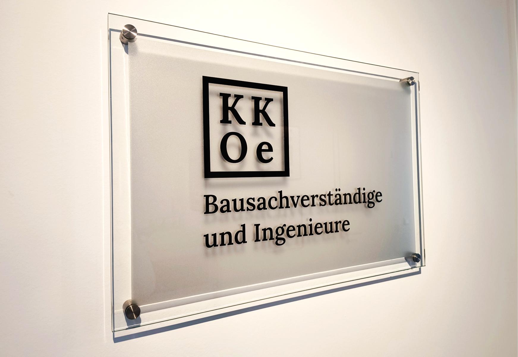 Das Bild zeigt das Firmenlogo des Ingenieurbüros (Düsseldorf) der KKOe Beratende Ingenieure Kempis Kleisa PartG mbB. Dieses hängt (in Form eines Glasschildes) an der Wand im Eingangsbereich des Unternehmens.